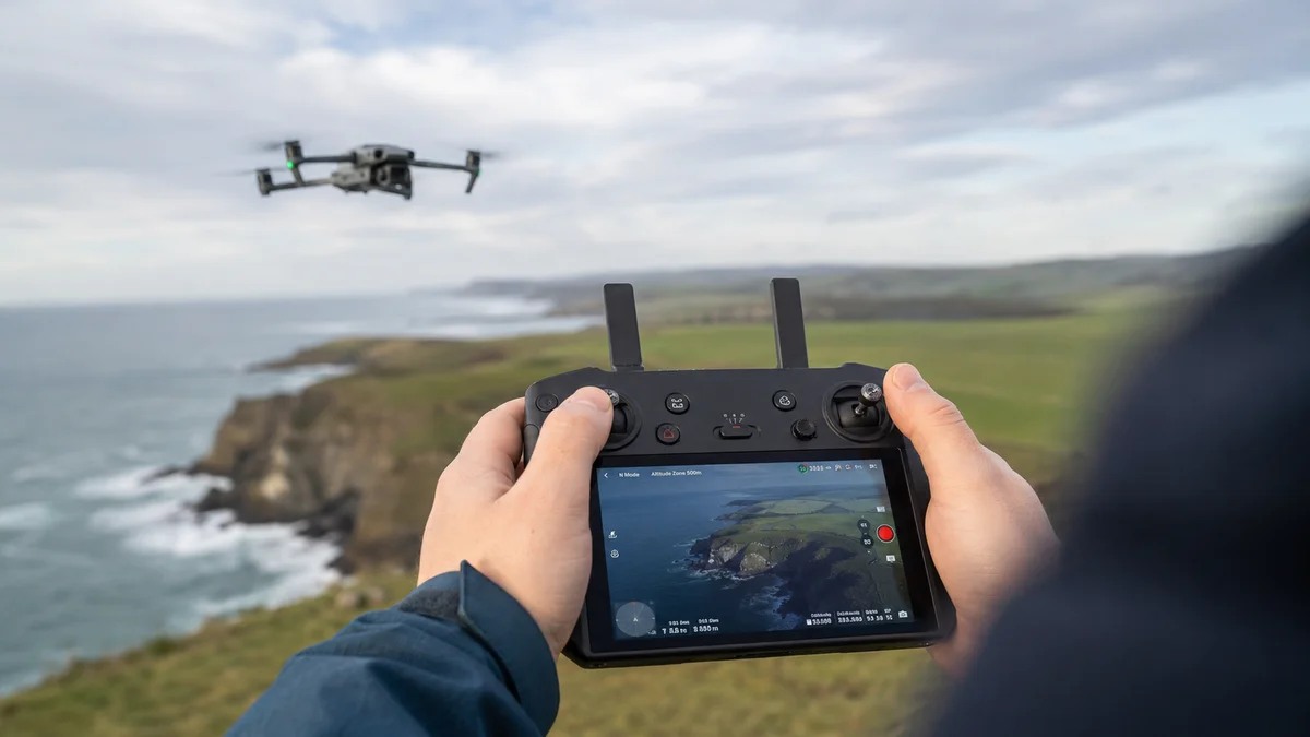 Drone pilot holding a controller with a live camera feed while the drone flies in the distance
