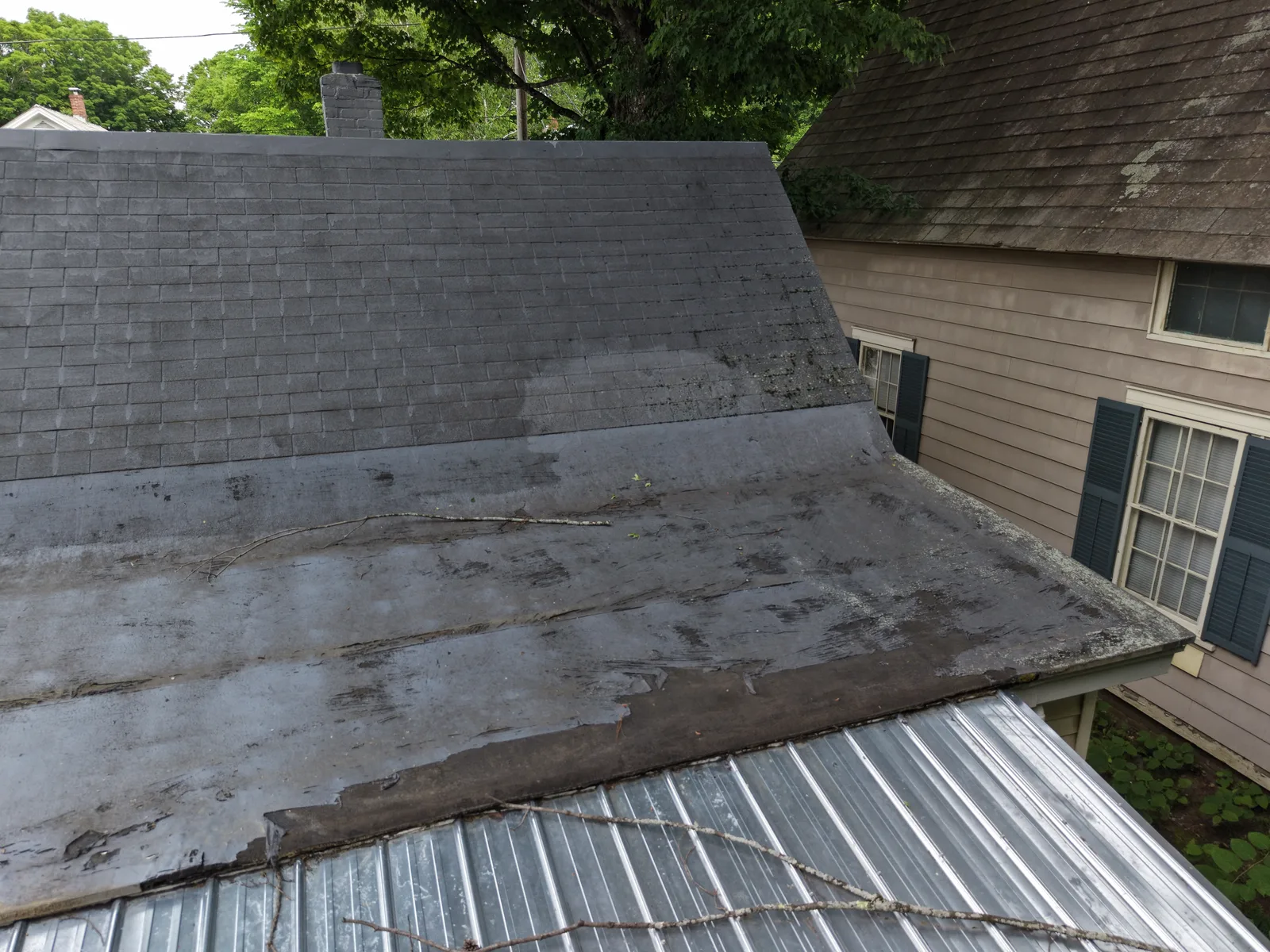 Drone angle showing shingle and flat roof transition with visible wear and surface detail — Brattleboro, VT