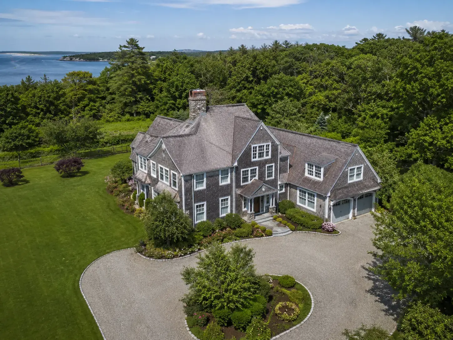 Aerial drone view of a coastal New England estate surrounded by trees and water
